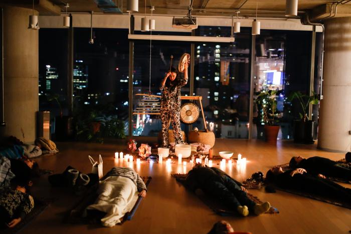 A veces lo único que necesitamos es parar. Frenar el ruido mental, bajar el ritmo del cuerpo y regalarnos un momento para volver a nosotros mismos. Esa es, en esencia, la propuesta de los baños de sonido que guía la periodista especializada en bienestar Belén Ortega. Una vez más tuvimos la oportunidad de participar de una de sus experiencias. Y la sensación inicial es bastante universal: uno llega cargando el cansancio del cuerpo, el estrés del día a día, las preocupaciones, las tensiones acumuladas y hasta esos pequeños dolores articulares que aparecen con los años —sobre todo cuando ya se cruzó la barrera de los 40. El equipo de Ortega recibe a los participantes con el espacio cuidadosamente preparado para propiciar un momento de pausa: luces suaves, aromas sutiles y una disposición de alfombras y colchonetas que invitan, casi de inmediato, a bajar el ritmo. De a poco, al recostarse, el cuerpo empieza a aflojar tensiones. La respiración se vuelve más consciente y también aparecen los pensamientos que llegan después de un día intenso. Pero a medida que los primeros sonidos comienzan a expandirse por el ambiente, algo cambia. Las vibraciones de los cuencos y los distintos instrumentos empiezan a envolver el espacio y no queda mucho por hacer más que entregarse a la experiencia. Qué es un baño de sonido Un baño de sonido es una experiencia de meditación guiada a través de vibraciones producidas por instrumentos ancestrales como cuencos tibetanos, cuencos de cuarzo, gongs y campanas armónicas. A diferencia de una clase tradicional de meditación, aquí el cuerpo “recibe” el sonido. Las frecuencias no solo se escuchan: también se perciben físicamente. “No se trata solo de escuchar música. El sonido trabaja sobre el sistema nervioso y permite que muchas personas alcancen un estado de calma que a veces no logran por sí solas”, explica Ortega. Qué sucede en el cerebro y el cuerpo Desde el punto de vista científico, la terapia de sonido se vincula con la forma en que ciertas frecuencias influyen en la actividad cerebral. “Científicamente el principio con el que trabajo es que ciertas frecuencias de sonido, medidas en Hertz (Hz), ayudan a ralentizar las ondas cerebrales. Favorecen la transición de ondas beta —asociadas al estrés, la hiperalerta y el pensamiento constante— hacia estados alfa y theta, que están vinculados con la relajación profunda, el foco interno, la creatividad y la recuperación del sistema nervioso”, señala. Este cambio de estado favorece la activación del sistema nervioso parasimpático, responsable de los procesos de descanso y recuperación del organismo. Cuando se activa, el cuerpo reduce la frecuencia cardíaca, disminuye la producción de cortisol —la hormona del estrés— y mejora la respiración. Para Ortega, su método también dialoga con saberes ancestrales que comprenden al cuerpo de una forma integral. “Este enfoque dialoga con tradiciones que entienden que los pensamientos no solo están en la mente, sino que también se sienten en el cuerpo: en los músculos, en la postura, en la respiración”. Una búsqueda que empezó hace más de 25 años La historia detrás de este método comenzó como una búsqueda personal. Durante más de dos décadas, mientras viajaba por el mundo entrevistando expertos en bienestar, Ortega buscaba también herramientas que la ayudaran a calmar su propia mente. “Buscaba técnicas que me ayudaran a bajar el ruido mental. Y solo lo encontré en el sonido durante un viaje a la selva maya”, recuerda. Ese hallazgo marcó un punto de inflexión. Desde entonces se formó en el exterior e investiga de manera permanente instrumentos, frecuencias y paisajes sonoros que influyen en el cerebro. Parte de su formación se desarrolló en Italia, España y comunidades mayas, donde profundizó en una tradición que entiende al cuerpo como un sistema de memoria fisiológica. “Es por eso que el sonido no solo busca relajar, sino modificar estados”, agrega. Un spa para el sistema nervioso Cada experiencia está pensada como un espacio donde el ruido mental disminuye y el cuerpo puede liberar tensiones acumuladas. Ortega trabaja con más de 50 instrumentos ancestrales, combinando frecuencias que actúan directamente sobre el sistema nervioso. “Cada instrumento tiene un efecto diferente sobre el cuerpo y las emociones”, explica. El objetivo final de estas experiencias es que los sonidos externos ayuden a reconectar con los sonidos internos: primero la respiración, luego los latidos del corazón y finalmente las palabras que cada persona se dice a sí misma. “Eso que nos decimos sin que nadie más escuche también es sonido y puede ser reparador o cargarnos de ansiedad”. Una práctica que gana espacio en el mundo El interés por el poder del sonido como herramienta de bienestar está creciendo en todo el mundo. Plataformas de streaming, aplicaciones de meditación y experiencias de spa comenzaron a incorporar paisajes sonoros y sesiones de relajación basadas en frecuencias. “No se trata de calmar la mente para reprimir pensamientos, sino de aprender a ser guardianes de nuestros propios pensamientos”, reflexiona Ortega. Próxima experiencia La próxima experiencia presencial guiada por Belén Ortega se realizará el sábado 14 de marzo a las 18:30 en el Hotel Casa Lucía, en la ciudad de Buenos Aires. Una membresía para llevar el sonido a la vida diaria Además de los encuentros presenciales, Ortega desarrolló una membresía online donde cada semana comparte sesiones de baños de sonido de 45 minutos. Las experiencias pueden realizarse en vivo los domingos a las 20 o accederse luego desde una biblioteca digital. “La idea es que las personas puedan usar el sonido cuando más lo necesitan: antes de dormir, al comenzar la mañana o incluso a mitad del día para recuperar energía”, explica. Una pausa necesaria Al terminar la sesión, el silencio se siente distinto. El cuerpo está más liviano, la respiración más profunda y la mente, por un momento, parece haber encontrado un nuevo ritmo. Tal vez ahí esté el verdadero sentido de la experiencia: recordar que, en medio del ruido constante del mundo, también existe la posibilidad de detenerse, escuchar y volver a encontrar calma.